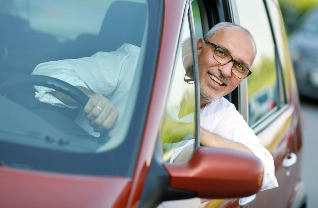 Adult with grey hair wearing glasses leaning out of driver's seat window while driving.